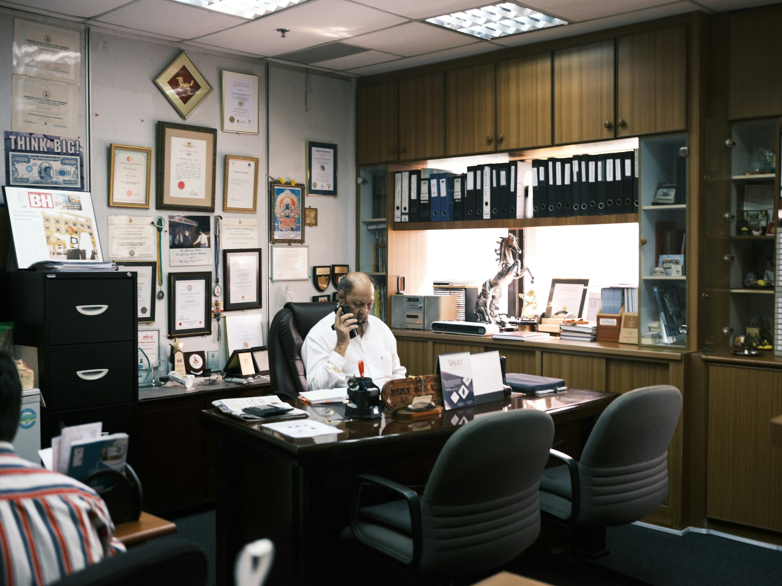 A person sitting at a desk surrounded by papers and a laptop, looking stressed about finances.